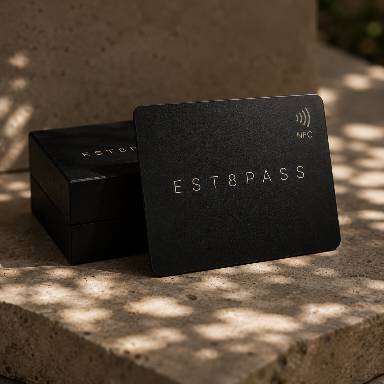 EST8PASS metal card leaning against its black gift box on stone